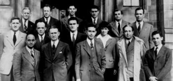 A group of people in suits standing in three rows on the steps in front of a stone building.