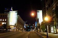 Illuminated buildings line a wide one-way city street at night